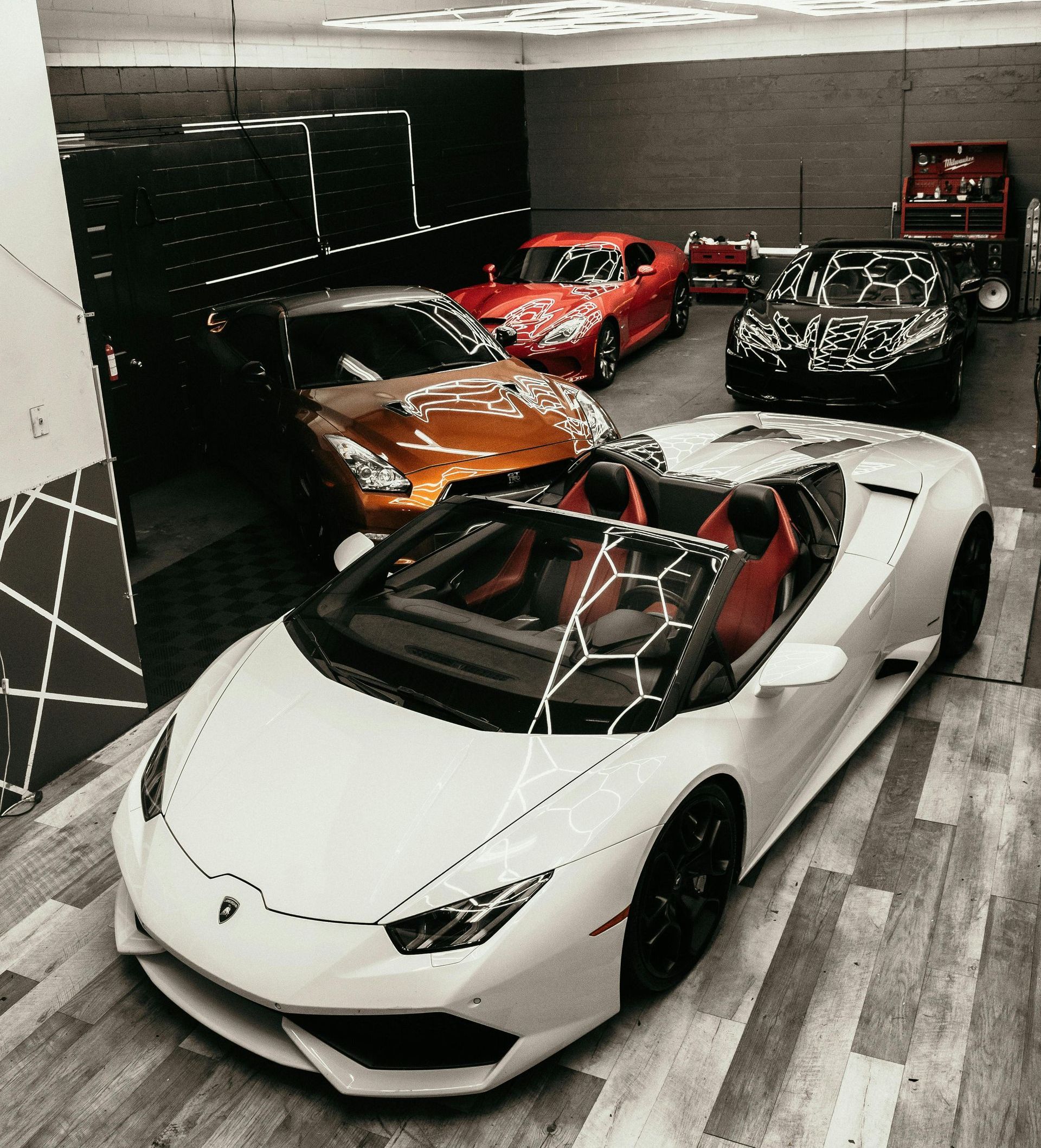 A white sports car is parked in a garage next to other cars.