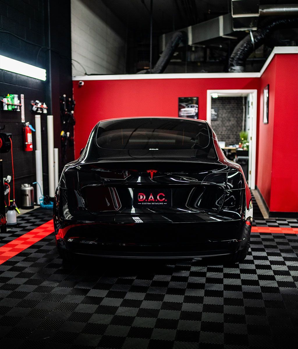 A black car is parked in a garage with red walls.