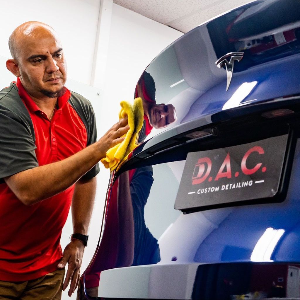 A man in a red shirt is cleaning a blue car with a yellow cloth.