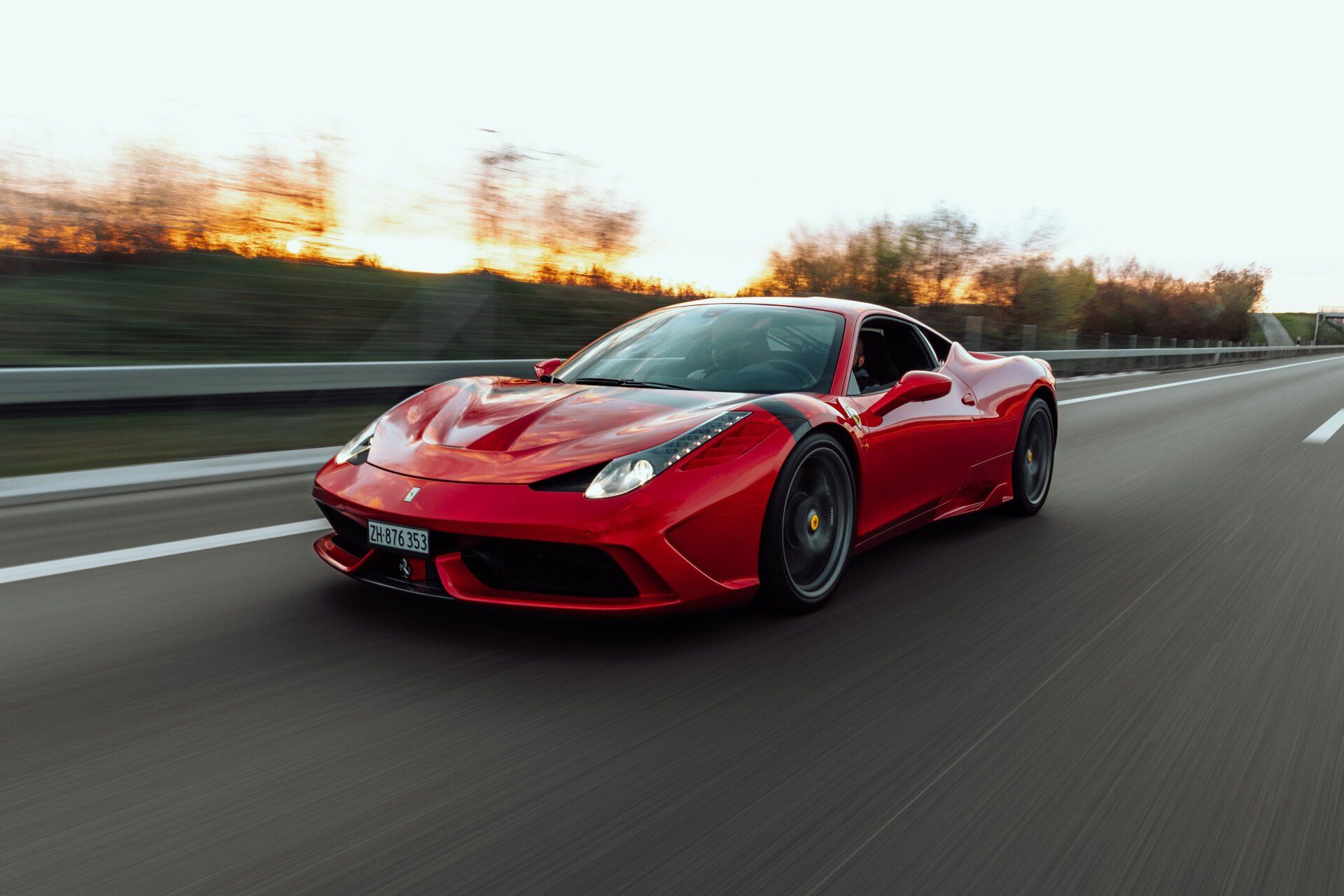 A red sports car is driving down a highway at sunset.