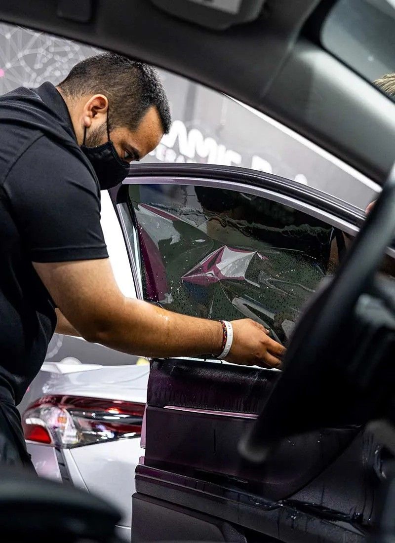 A man wearing a mask is working on a car window.