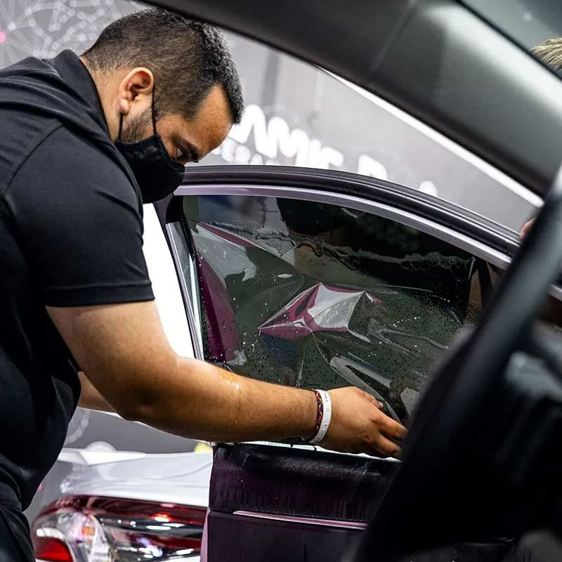 A man wearing a mask is working on a car window.