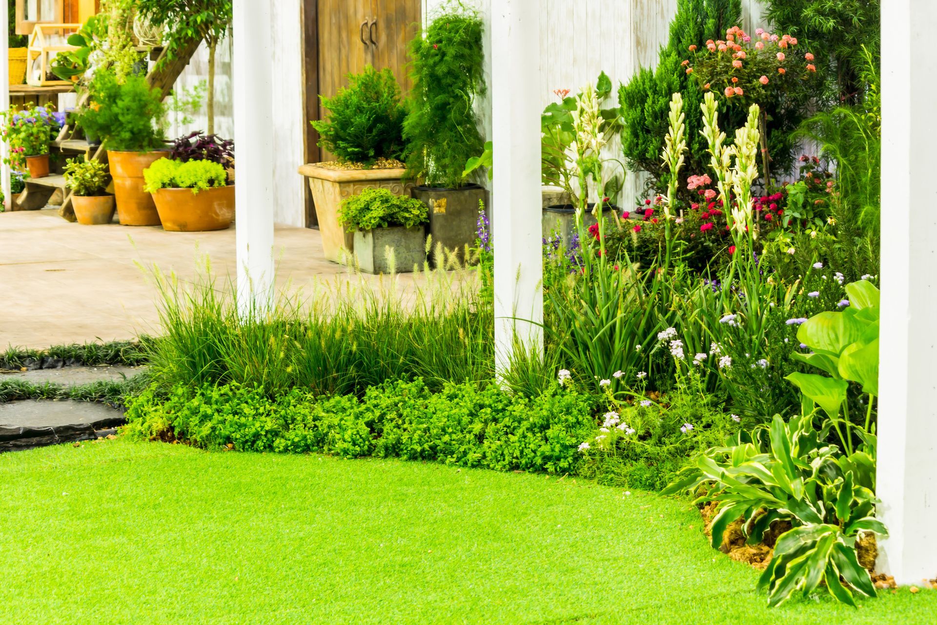 A lush green garden with potted plants and flowers in front of a house.