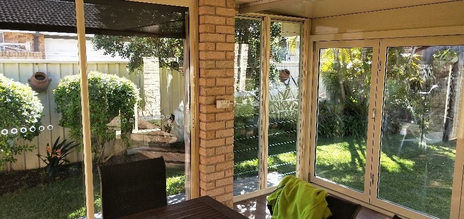 A Screened in Porch With a Table and Chairs and a View of a Garden — Superior Windows & Doors Taree,