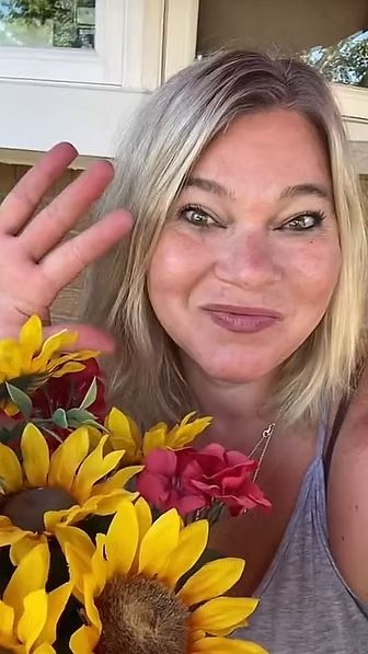 A woman is holding a bouquet of sunflowers and waving at the camera.
