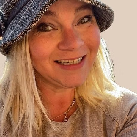 A woman wearing a hat and a necklace is smiling.