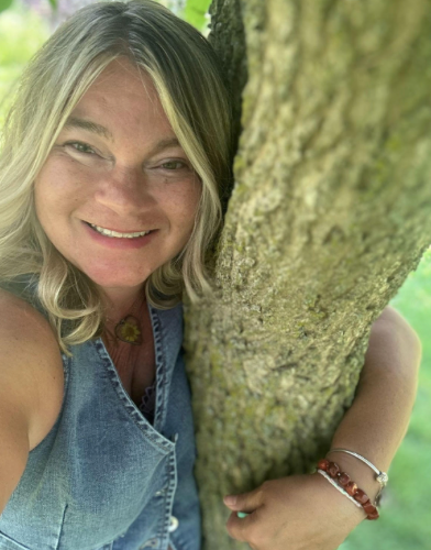 A woman is hugging a tree and smiling while taking a selfie.