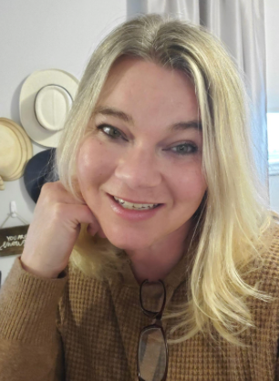 A woman wearing a brown sweater is smiling for the camera.