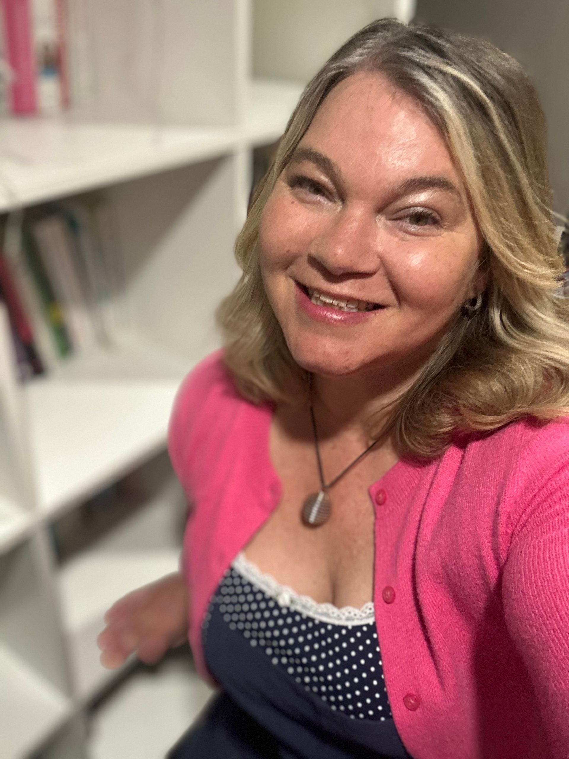 A woman in a pink cardigan is smiling for the camera.