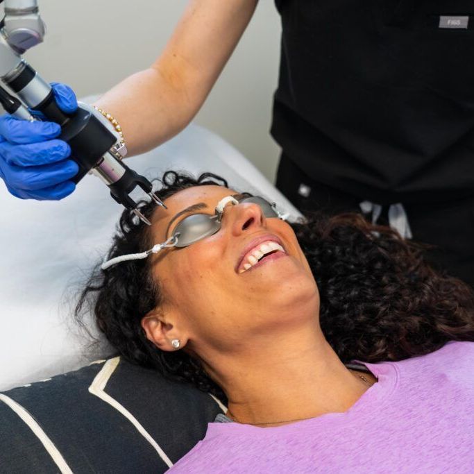 A woman is smiling while getting a laser treatment on her face.