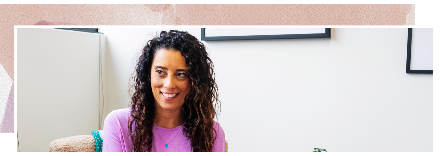 A woman with curly hair is sitting in a chair and smiling.