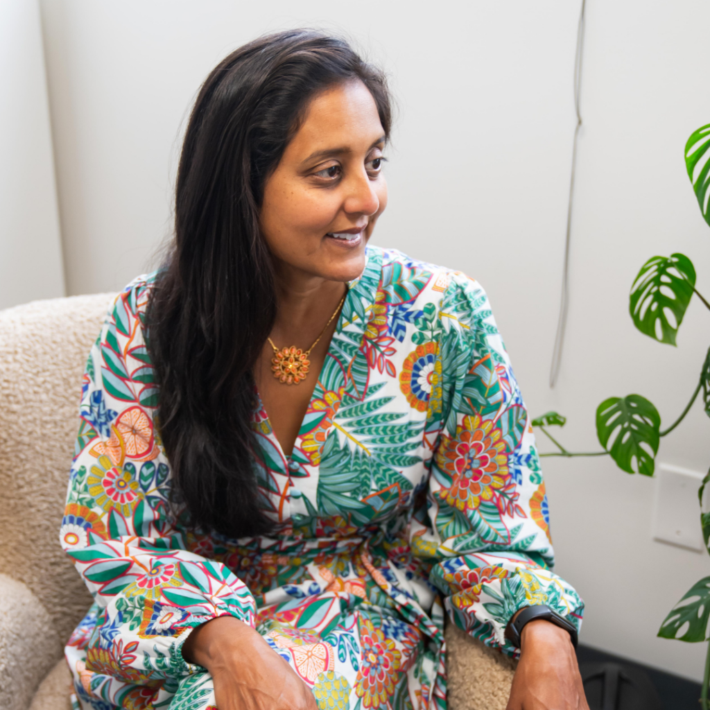 A woman in a colorful dress is sitting in a chair next to a plant.