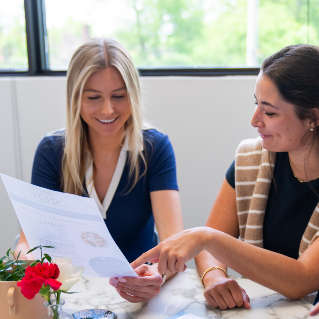 Two women are sitting at a table looking at a piece of paper.