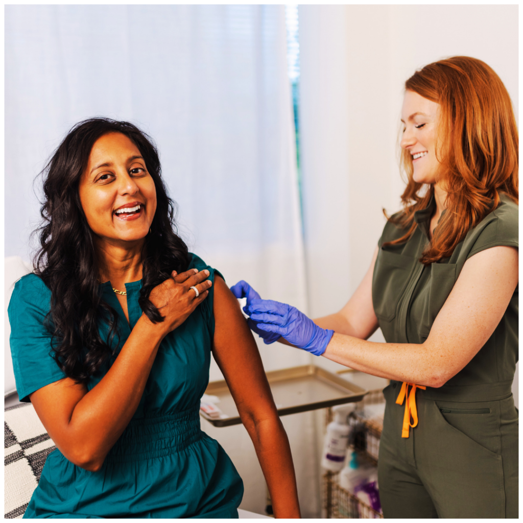 A woman is smiling while getting a vaccine from a nurse.