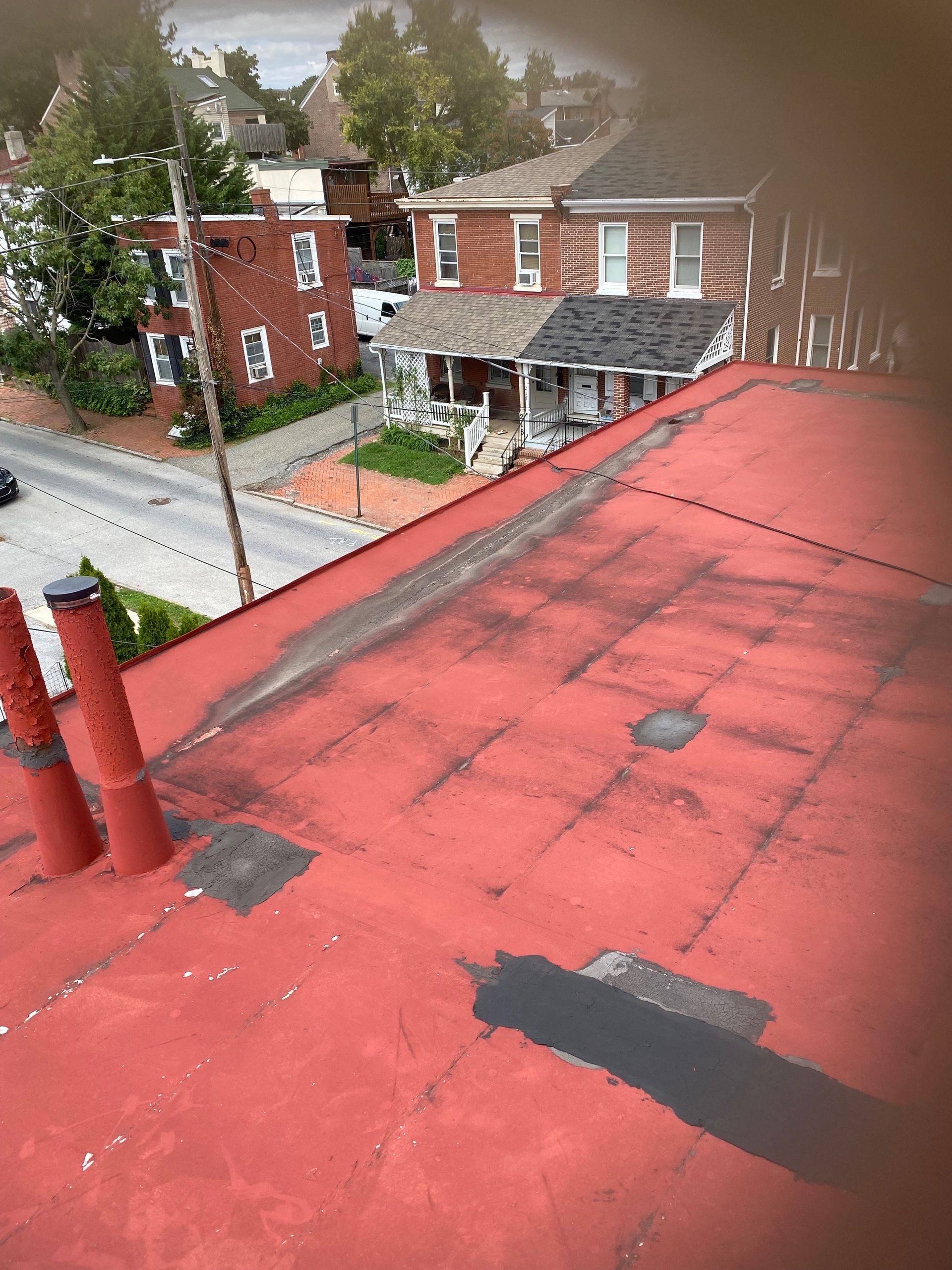 A red roof with a chimney on it and a house in the background.