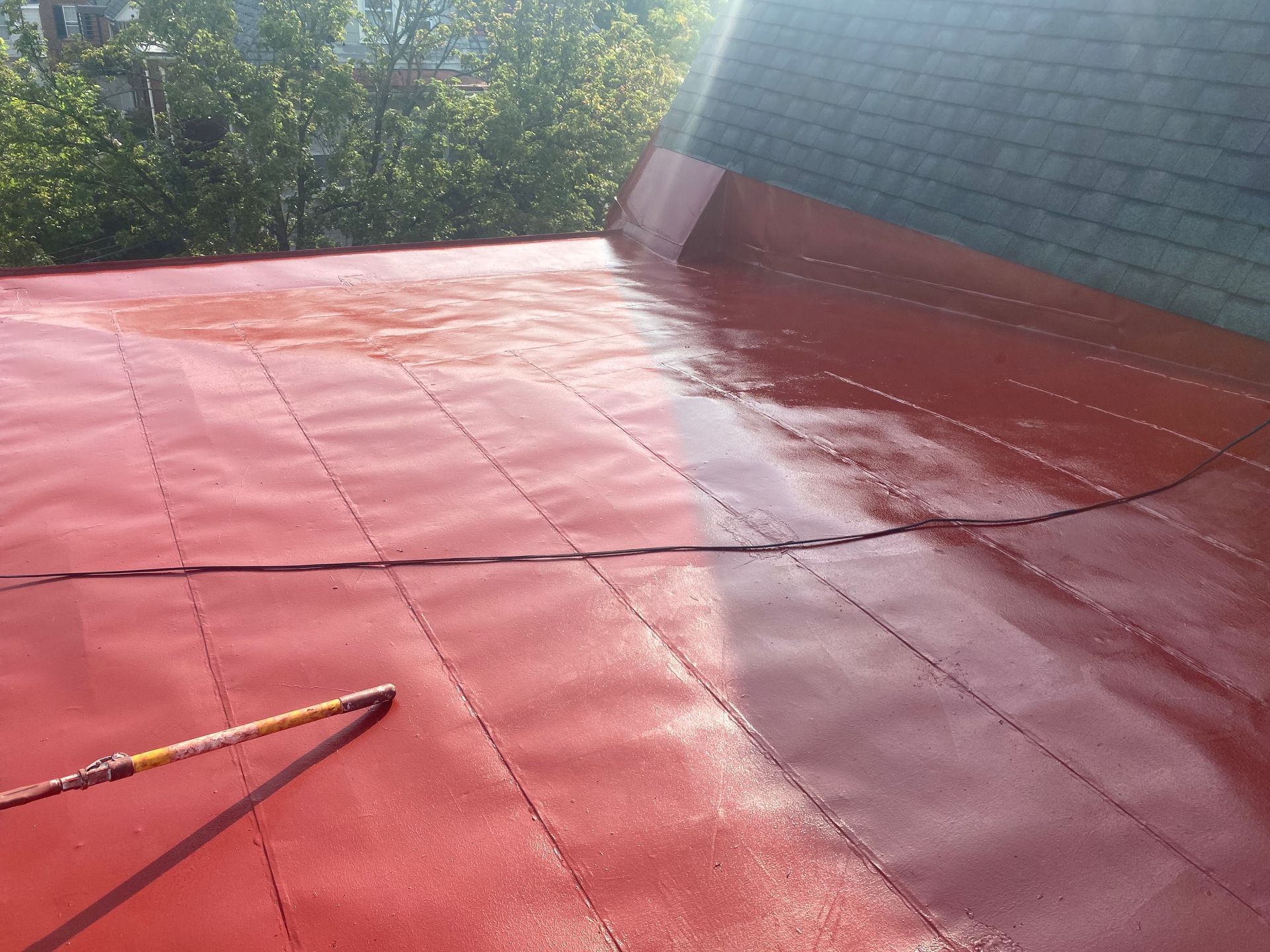 A person is painting a red roof with a roller.
