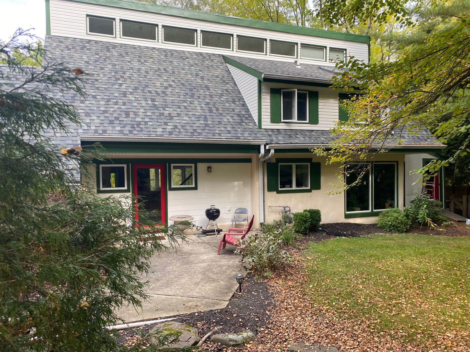 A large white house with green shutters and a red door is surrounded by trees.