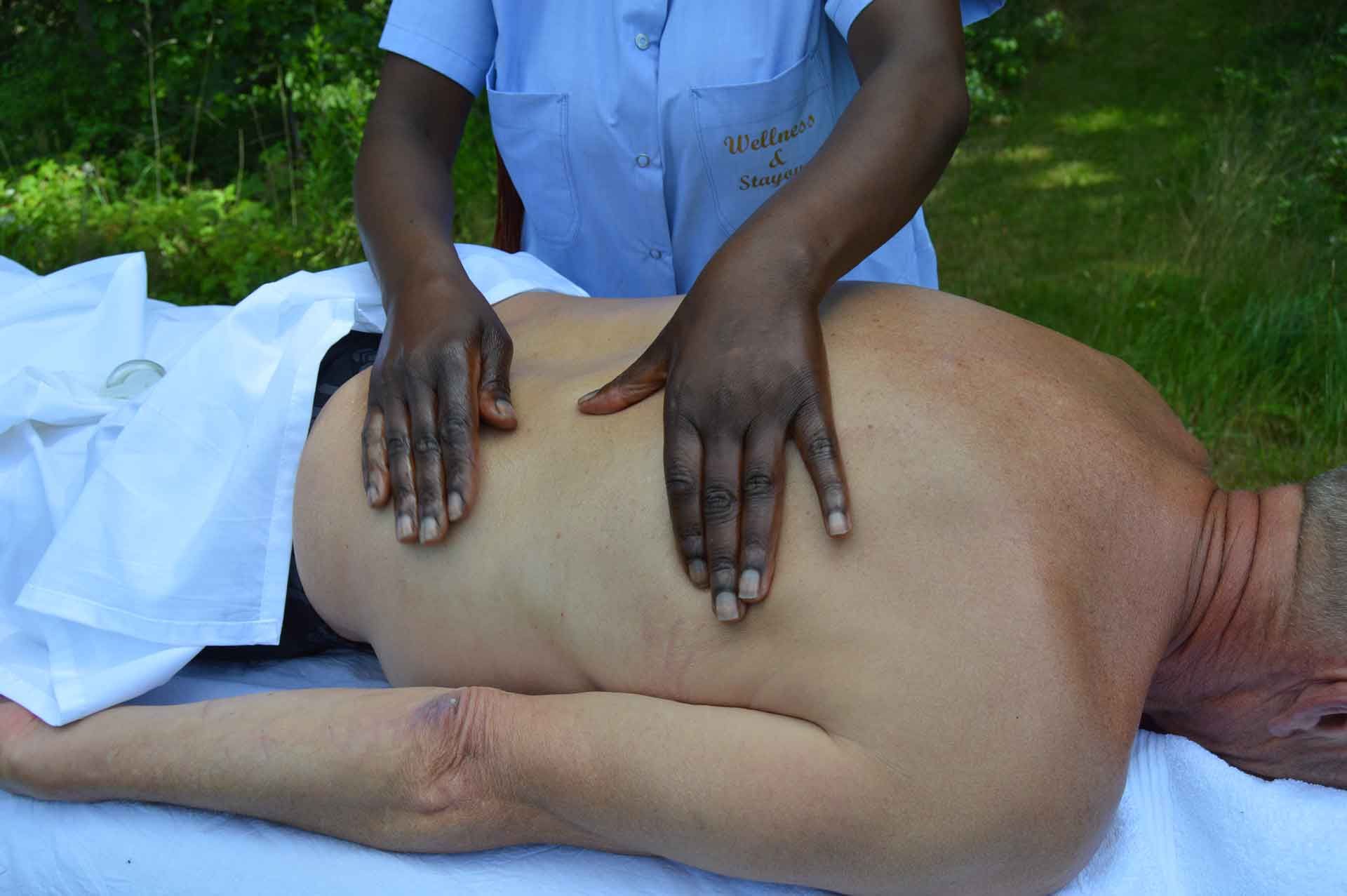 Person modtager rygmassage udendørs. En massør presser hænderne ind i mandens ryg.