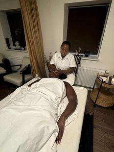 Person, der hælder olie på sin hånd, ligger på et bord og er ved at massere en andens ryg. Dæmpet belysning, stearinlys.