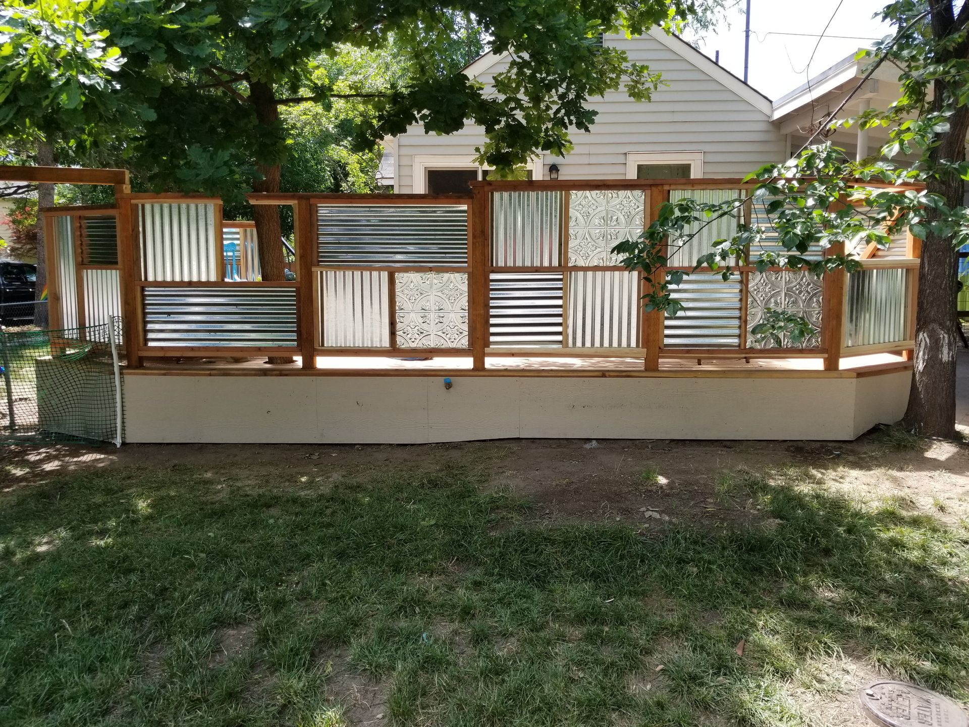 A wooden fence made of corrugated metal and glass is in front of a house.
