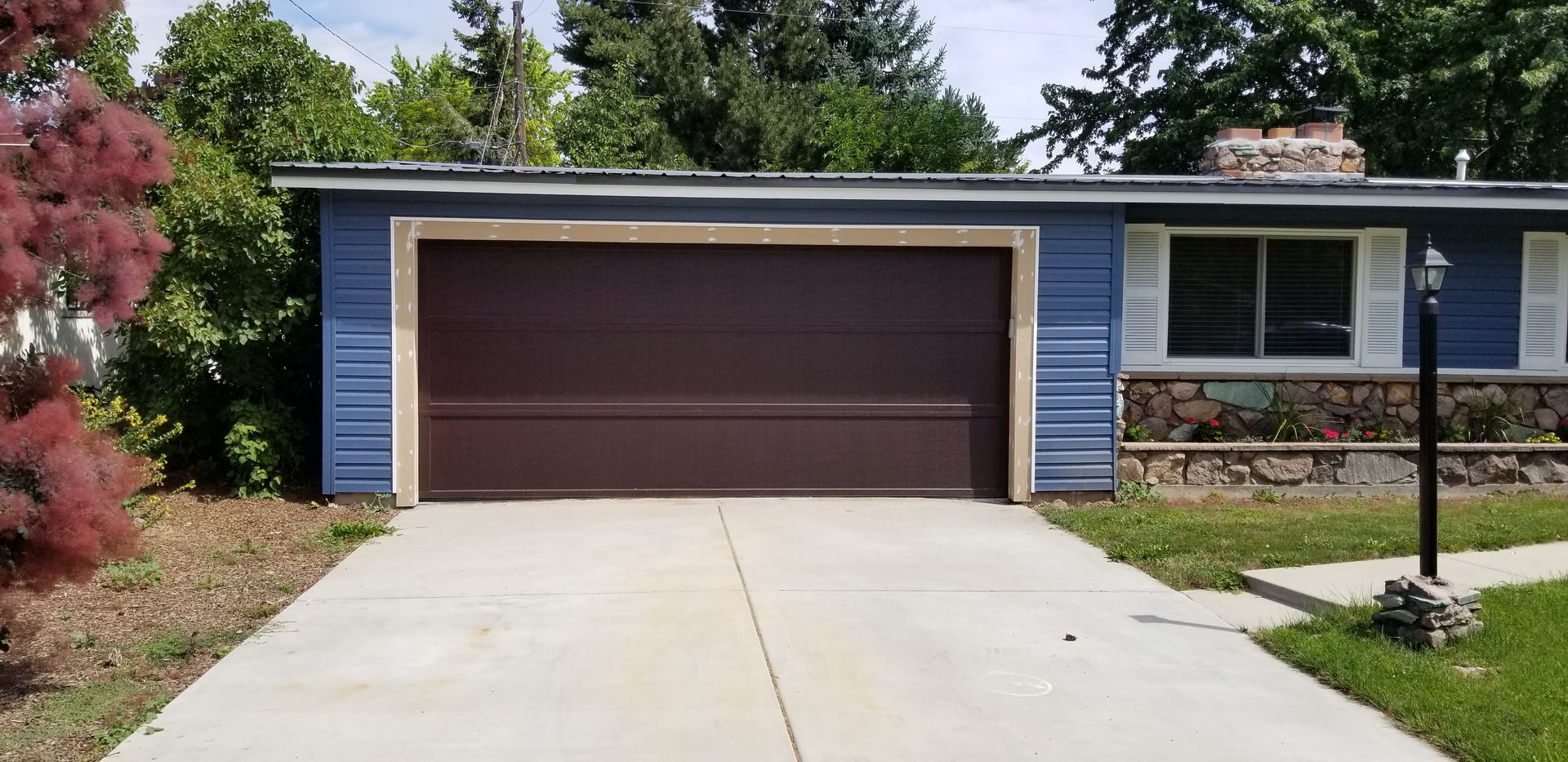 A blue house with a brown garage door and a concrete driveway.