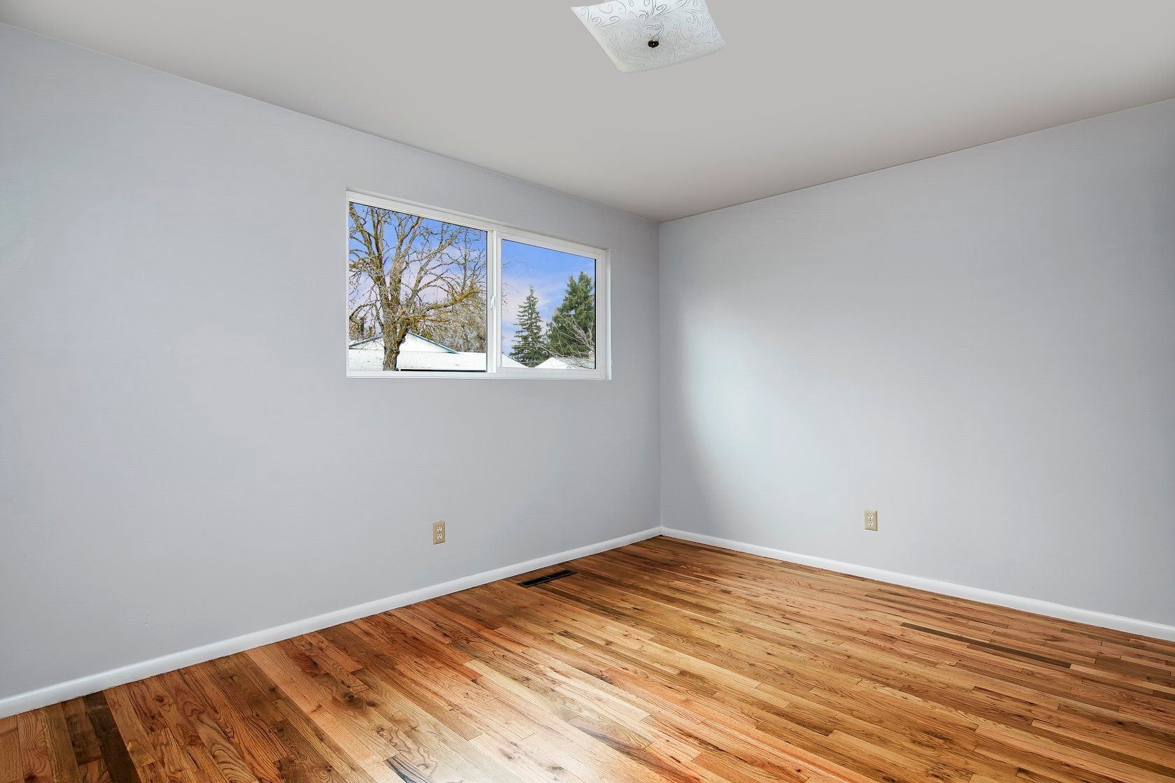 An empty room with hardwood floors and a window.