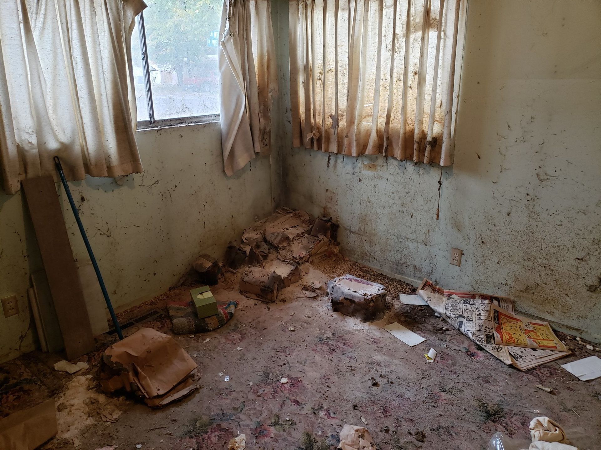 A dirty room with a window and a lot of trash on the floor.