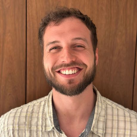 A man with a beard is smiling and wearing a plaid shirt.