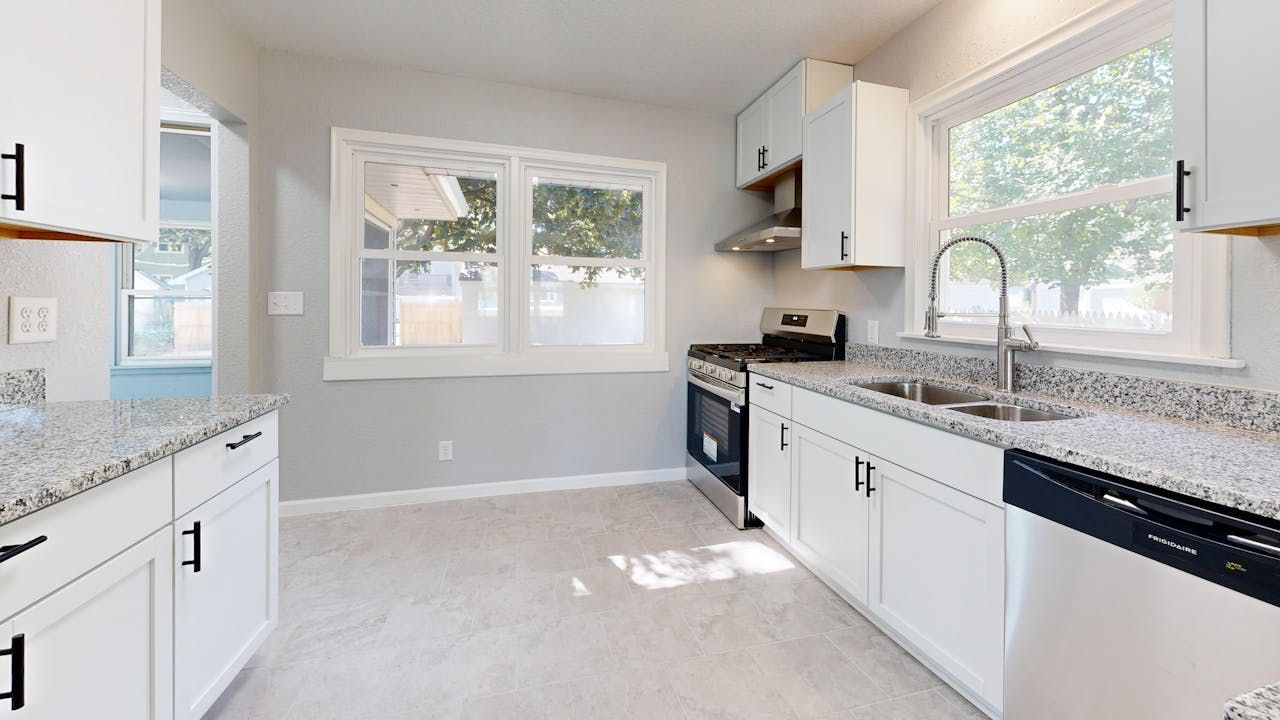 Sunlit modern kitchen featuring granite countertops and sleek white cabinetry.
