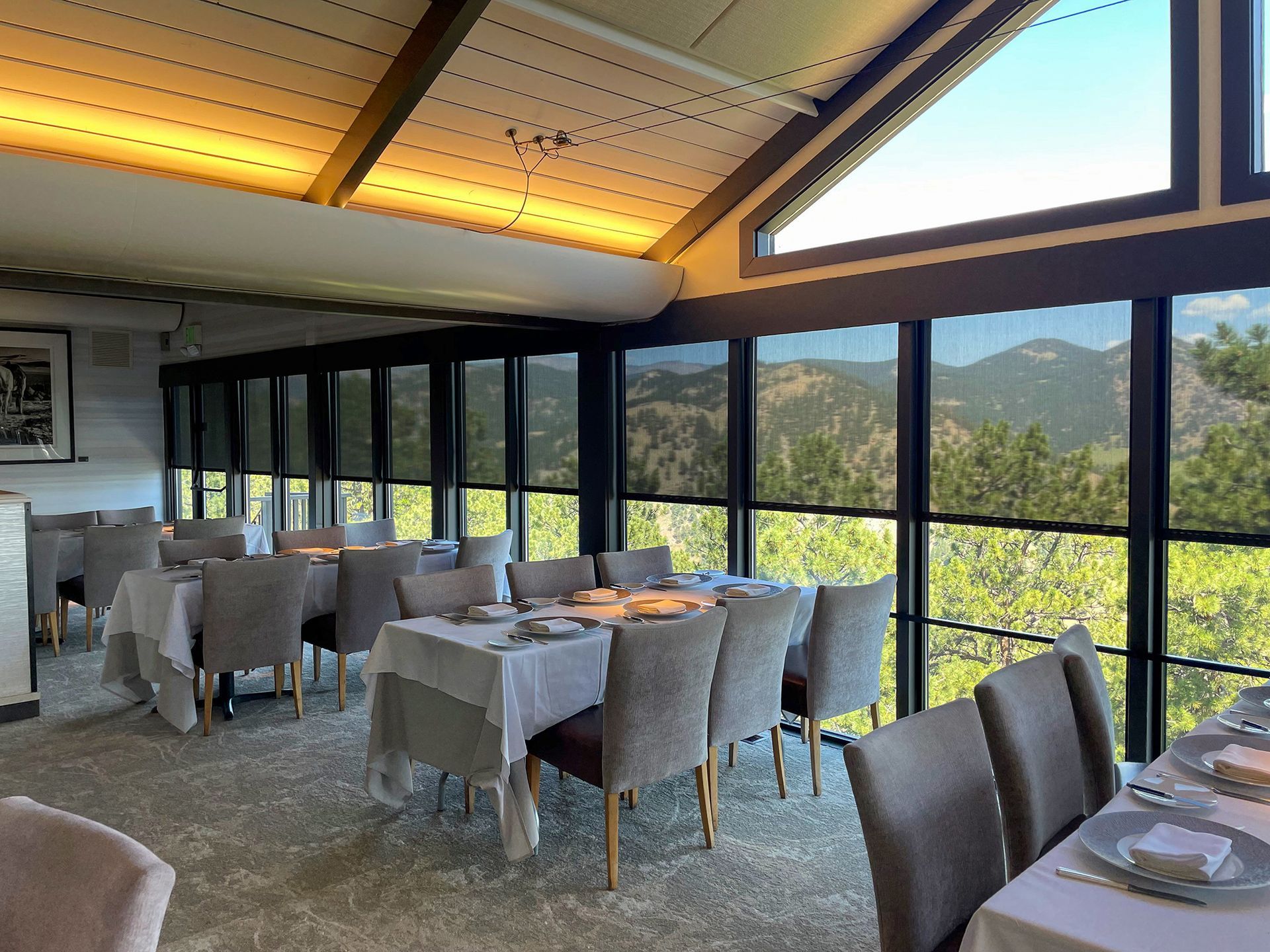 Dining room with tables set for a meal, large windows with a mountain view, and modern chairs.