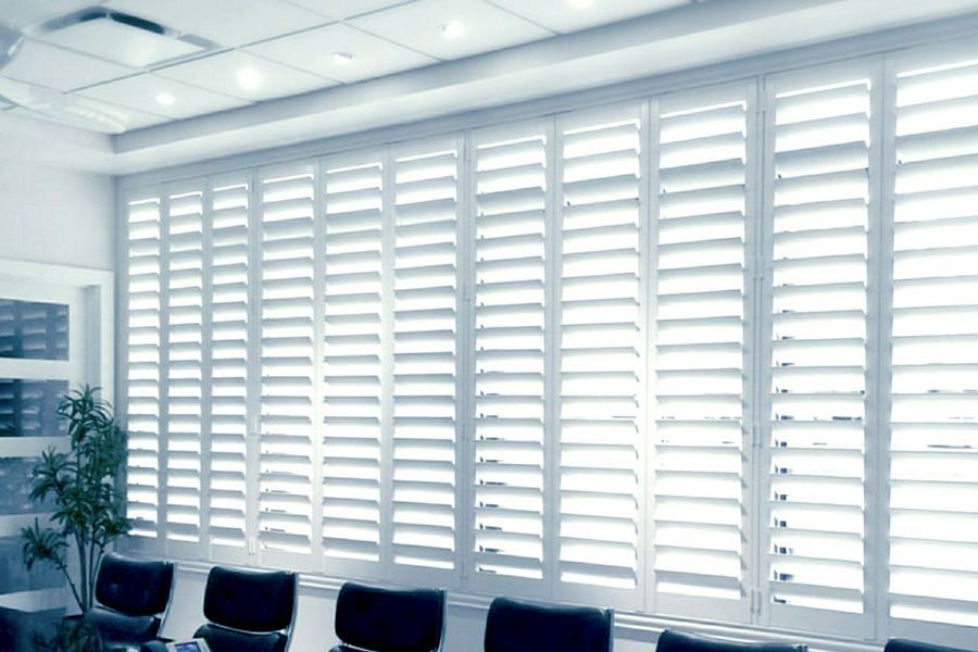 White window shutters on a wall, filtering sunlight in an office setting.
