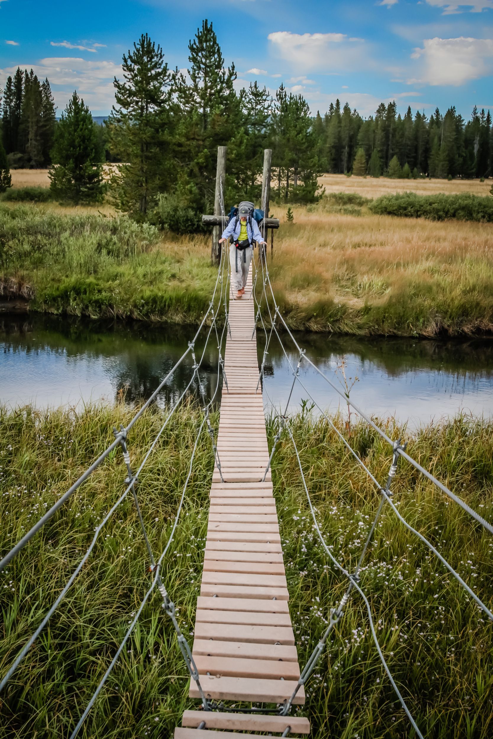 A backpacker cautiously navigates a swinging bridge in the Bechler Meadows area of Southwestern Yellowstone.