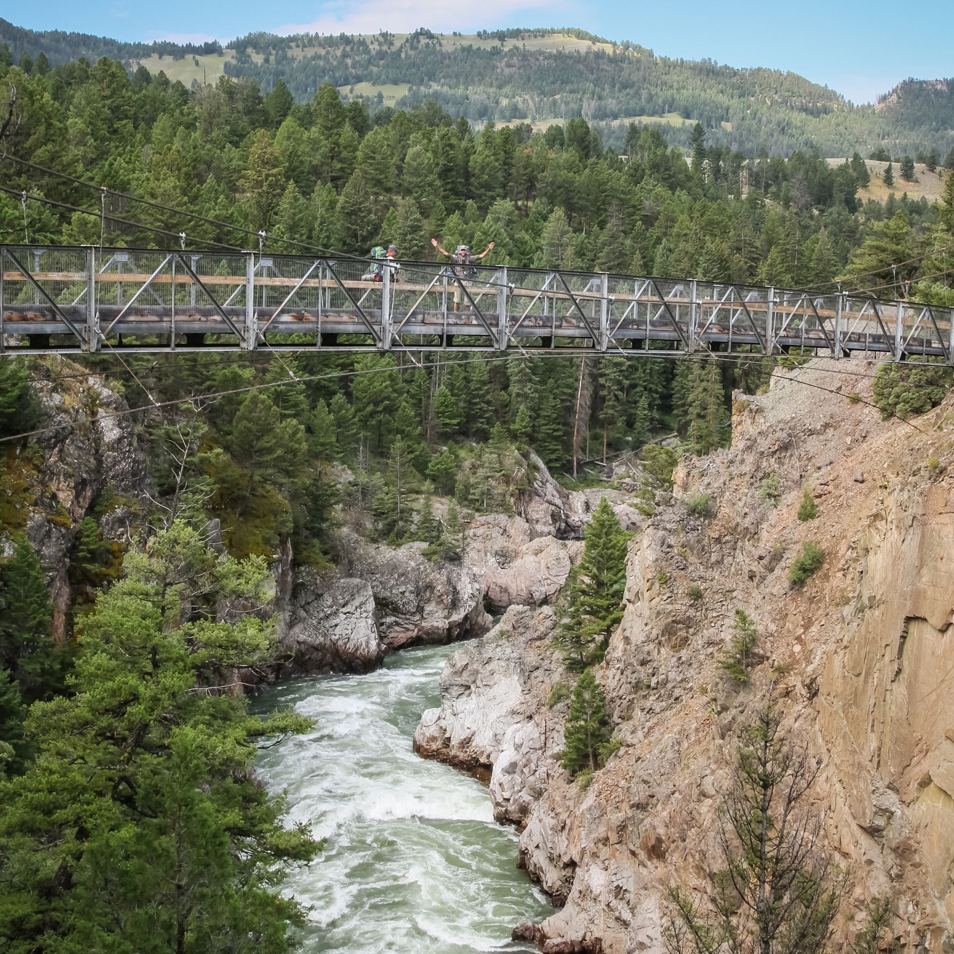 Backpackers stop for a photo on a suspension bridge located high above the Yellowstone River.