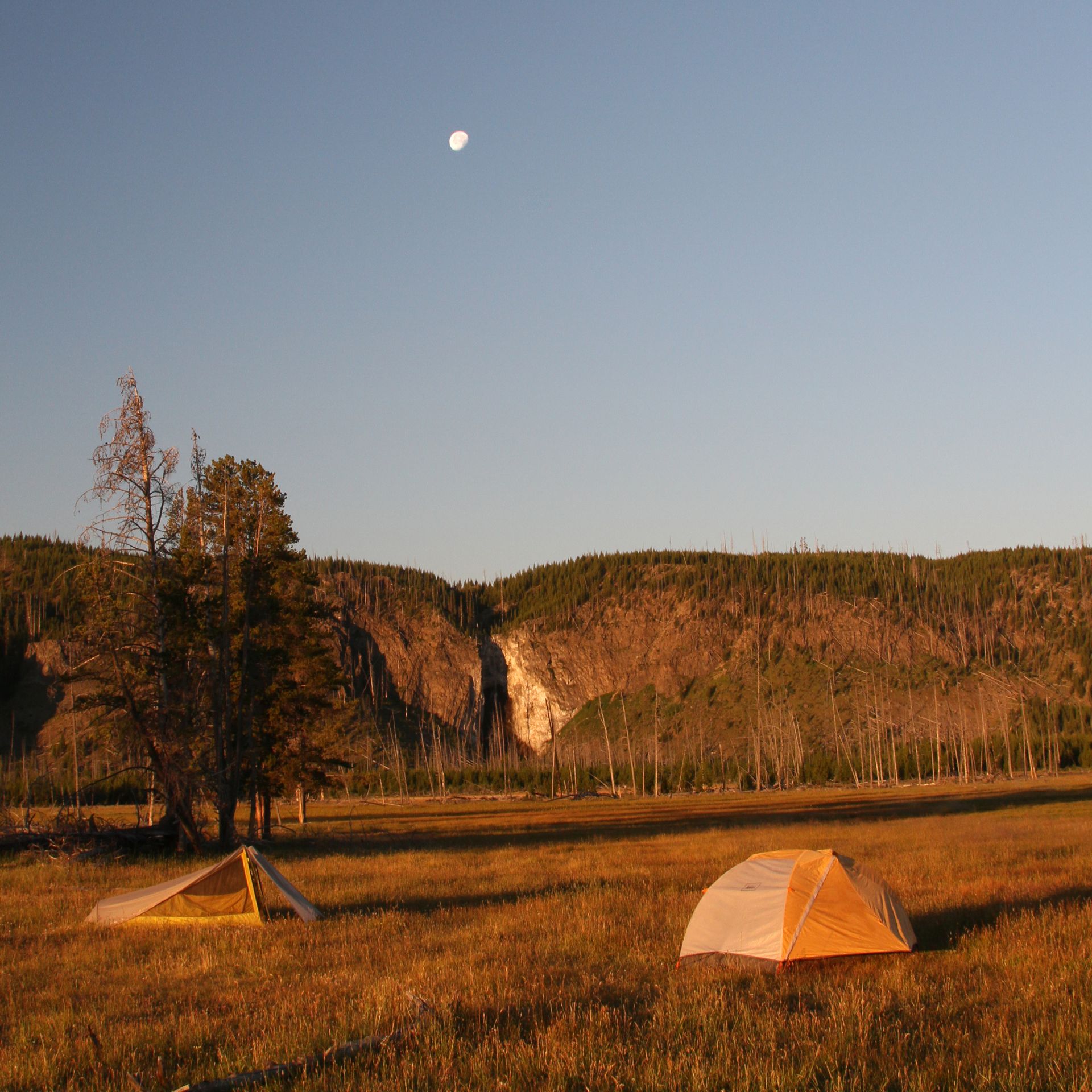 The moon rises over Fairy Falls as the morning sun casts a beautiful orange glow across the landscape.