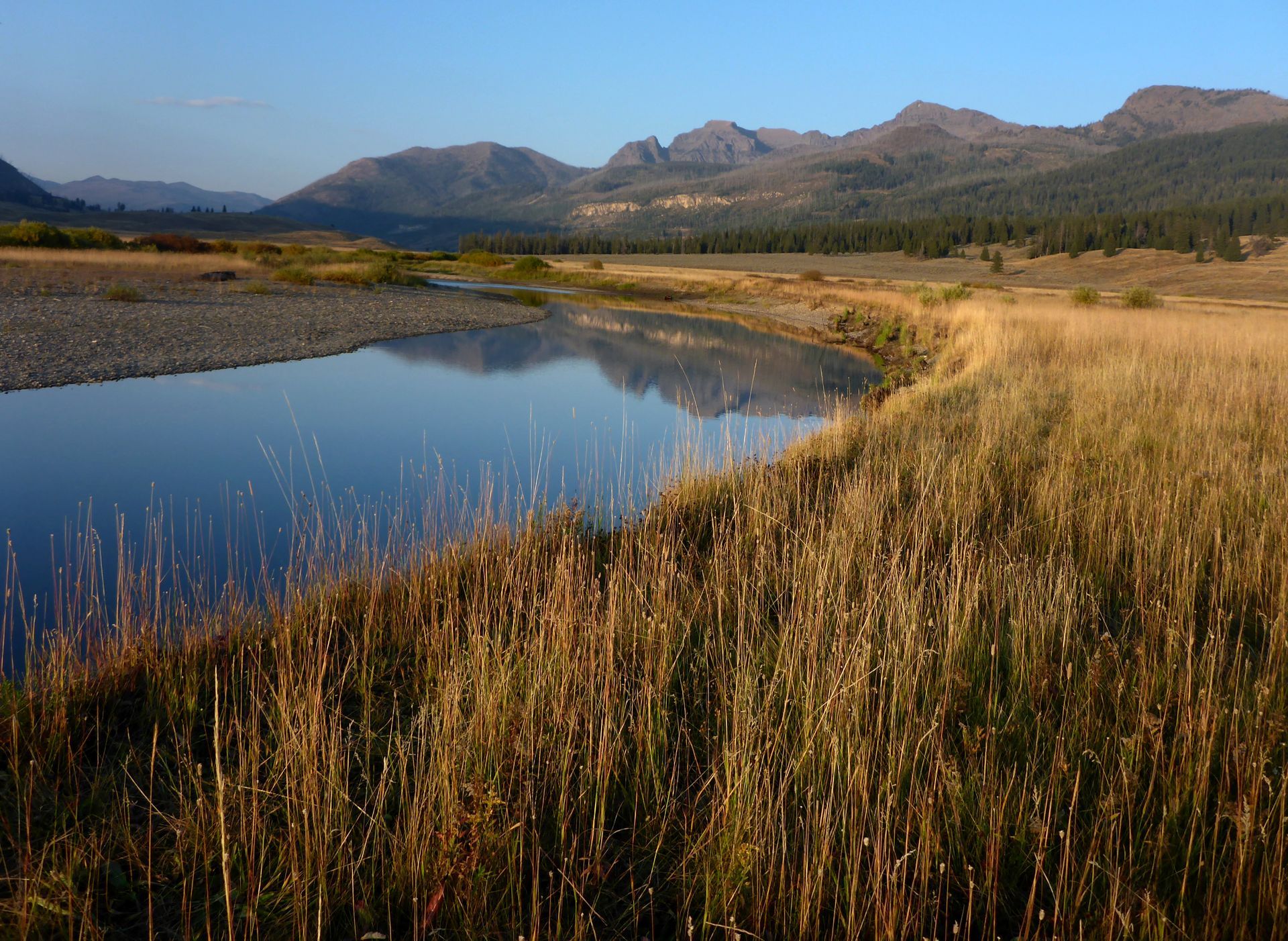 A calm stretch of water along Slough Creek reflects the towering peaks of Cutoff and Sugarloaf mountains.