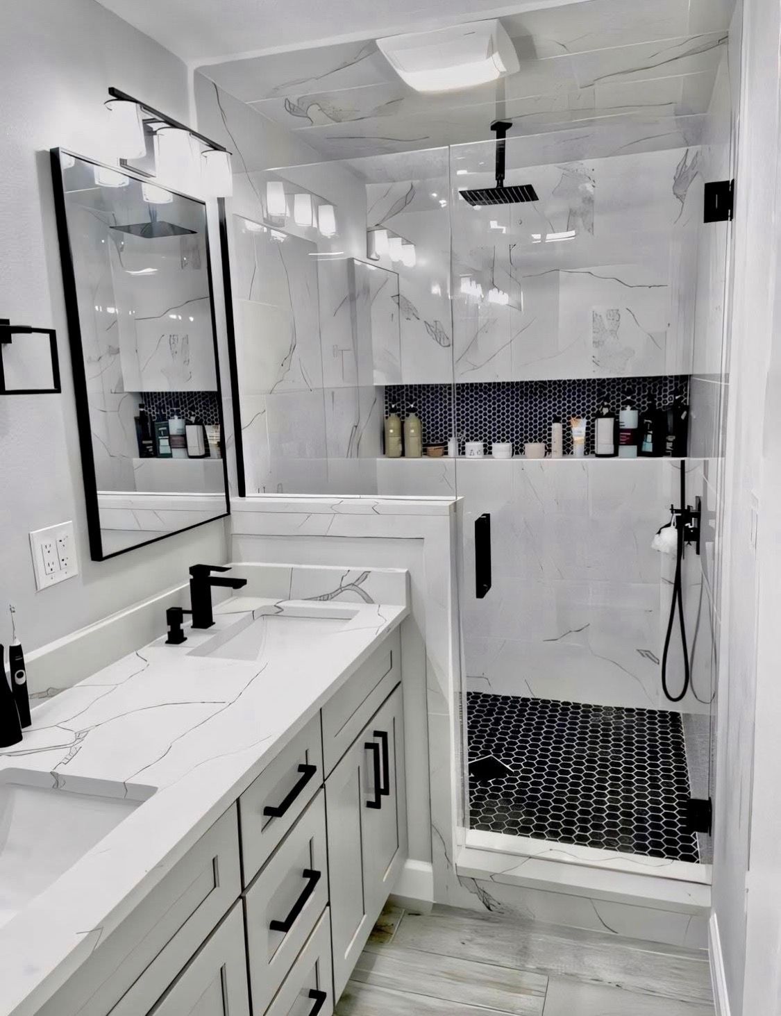 Modern bathroom with a marble-topped white vanity, black hardware, a black-framed mirror, and a walk-in shower.