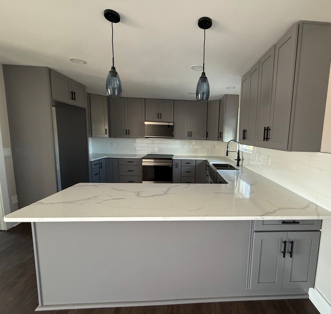 Modern kitchen featuring gray cabinets, white marble countertops, a central island, and two pendant lights overhead.