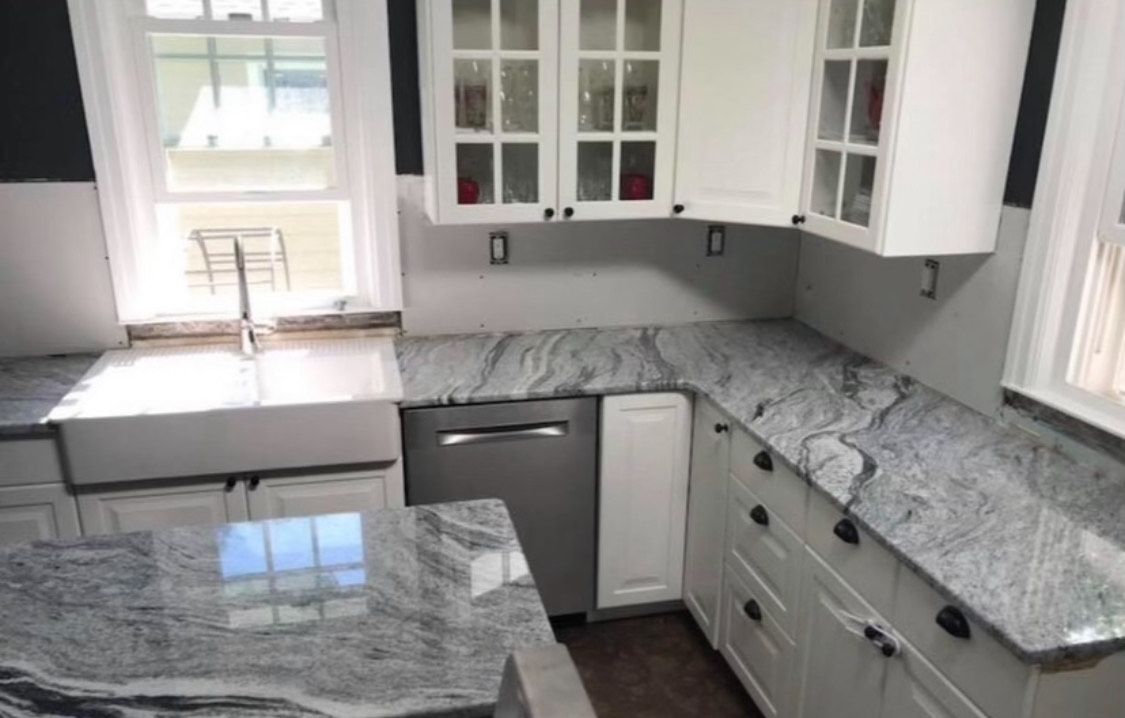 A kitchen with white cabinets , granite counter tops , a sink , and a dishwasher.