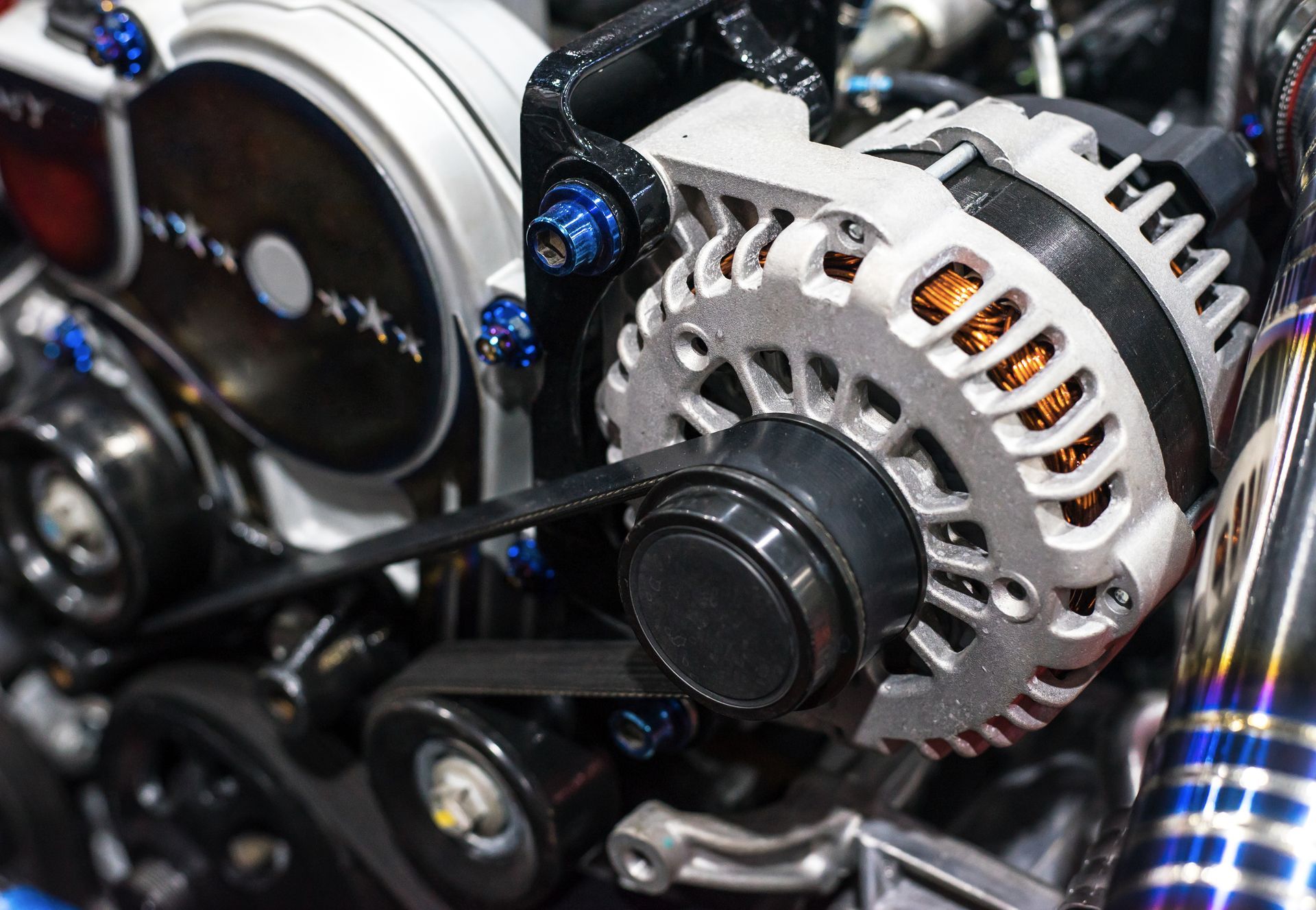 Close-up of a car engine alternator and belt drive with metal components and blue accents | Cruz-N-Carz