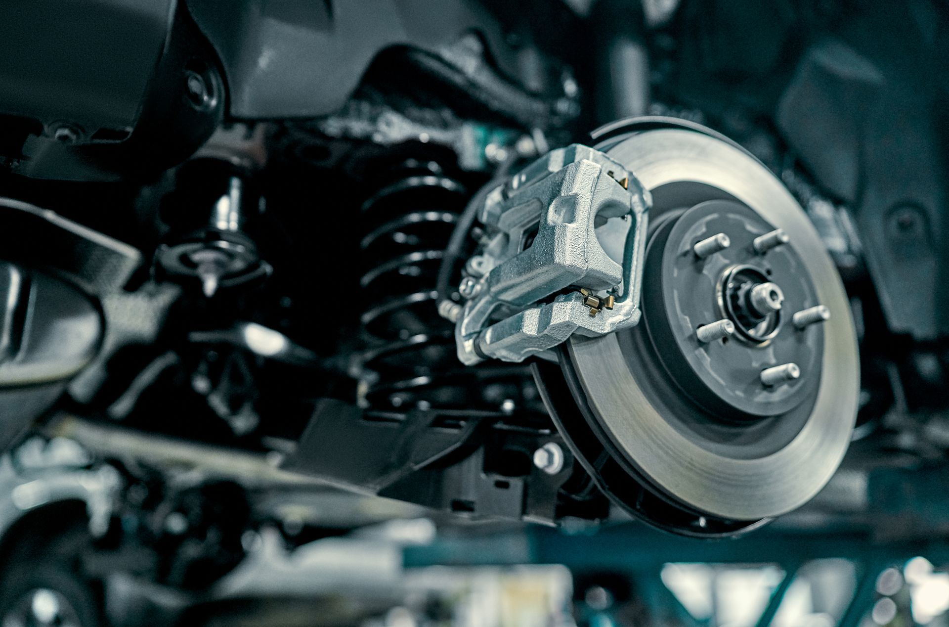 Car brake rotor and caliper with suspension components in a workshop close-up | Cruz-N-Carz