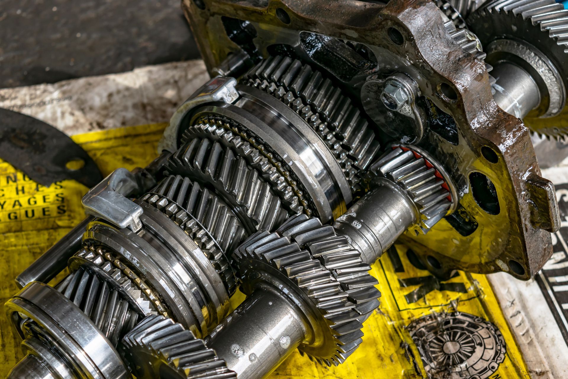 Exposed metal gearbox with gears and shafts on a yellow workbench, covered in grease and grime | Cruz-N-Carz