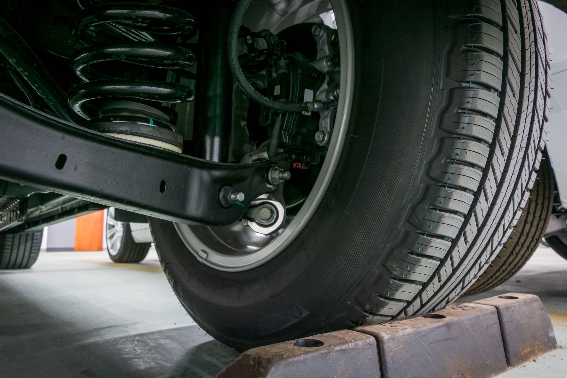 Close-up of a car wheel and suspension resting on a wheel chock in a garage. | Cruz-N-Carz