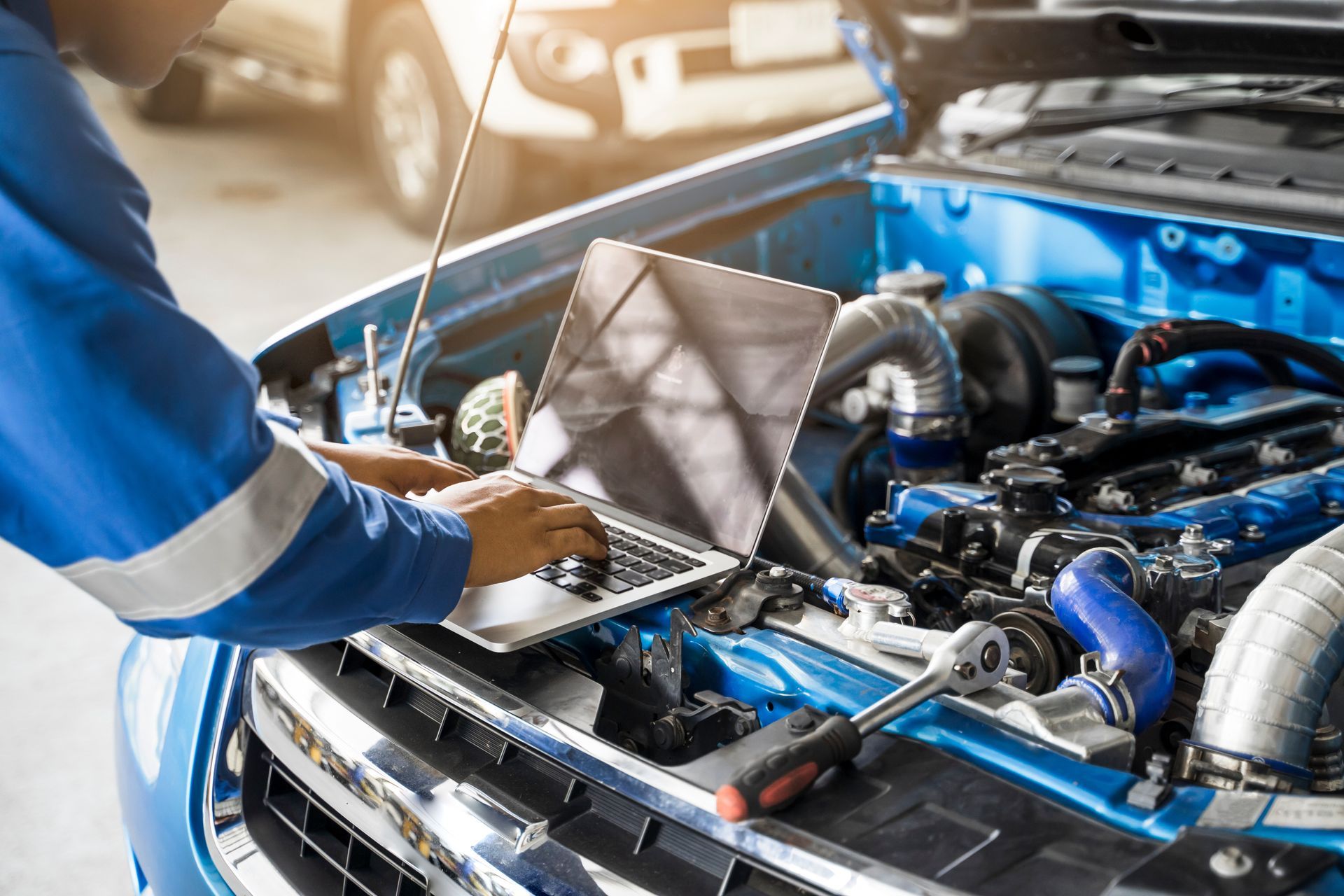 Mechanic using a laptop to diagnose a blue car’s open engine bay | Cruz-N-Carz