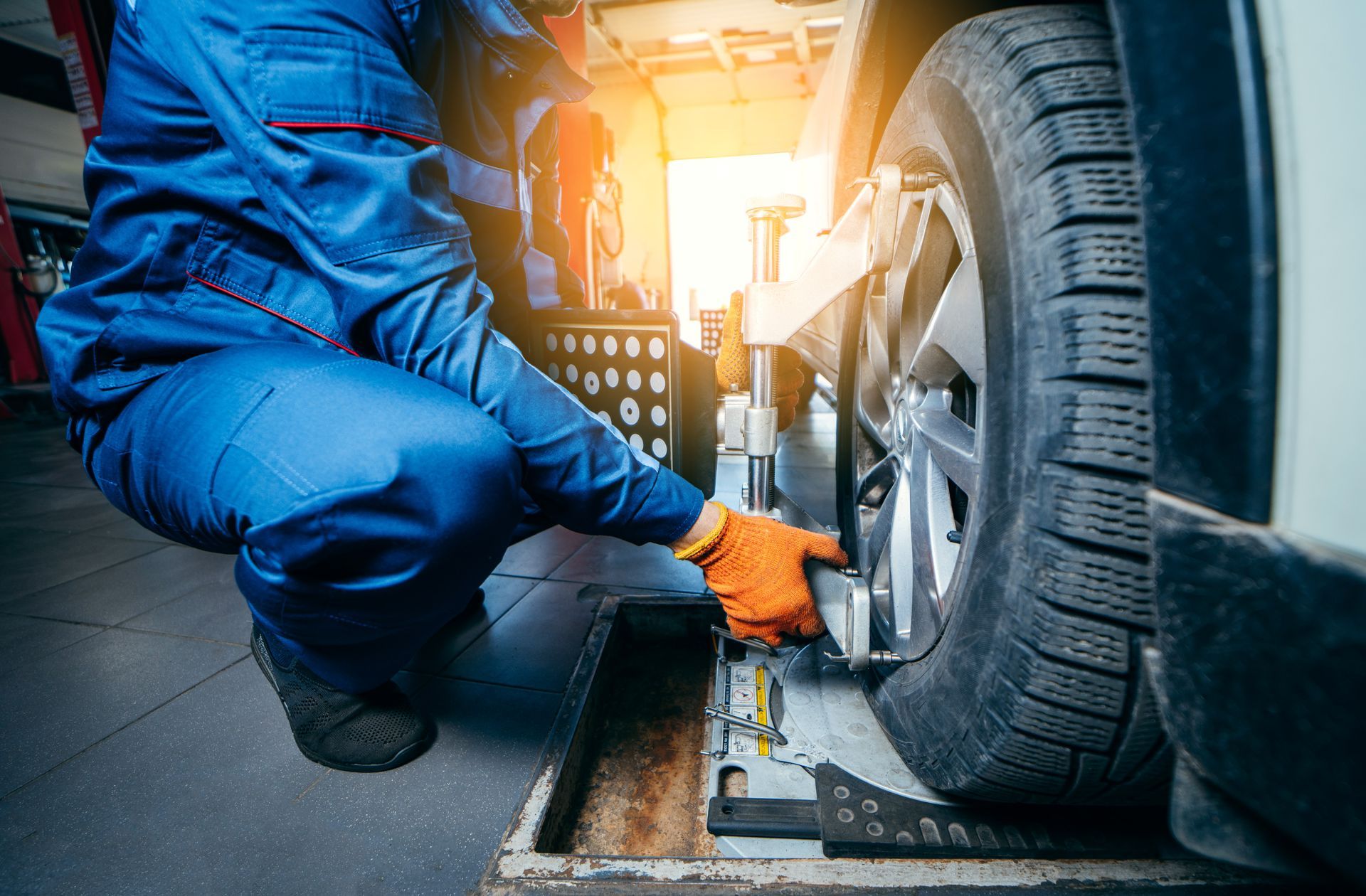 Mechanic in blue coveralls inspects a car tire with a wrench under bright garage lights | Cruz-N-Carz