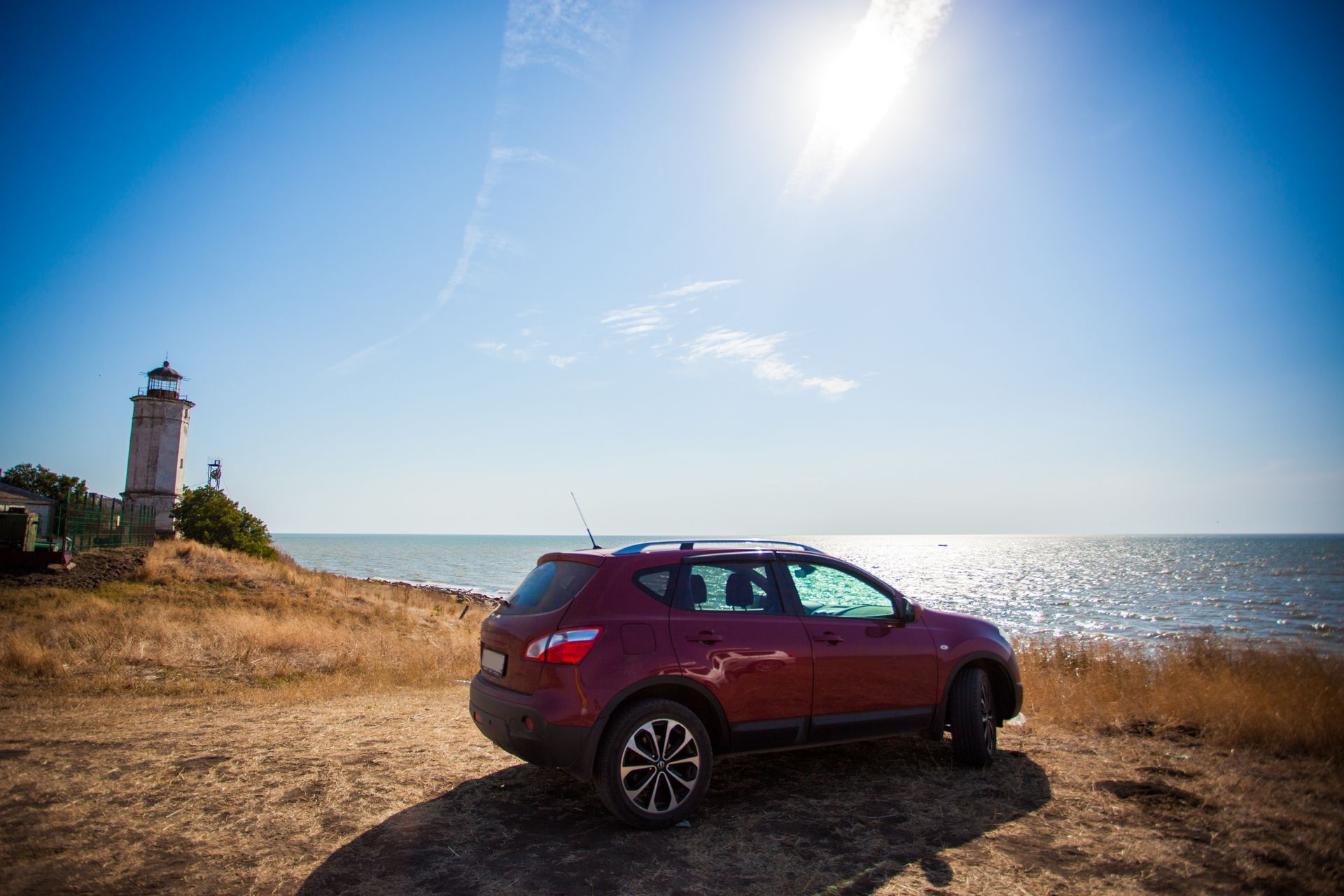 Red SUV parked by the coast near a lighthouse under a bright sun | Cruz-N-Carz