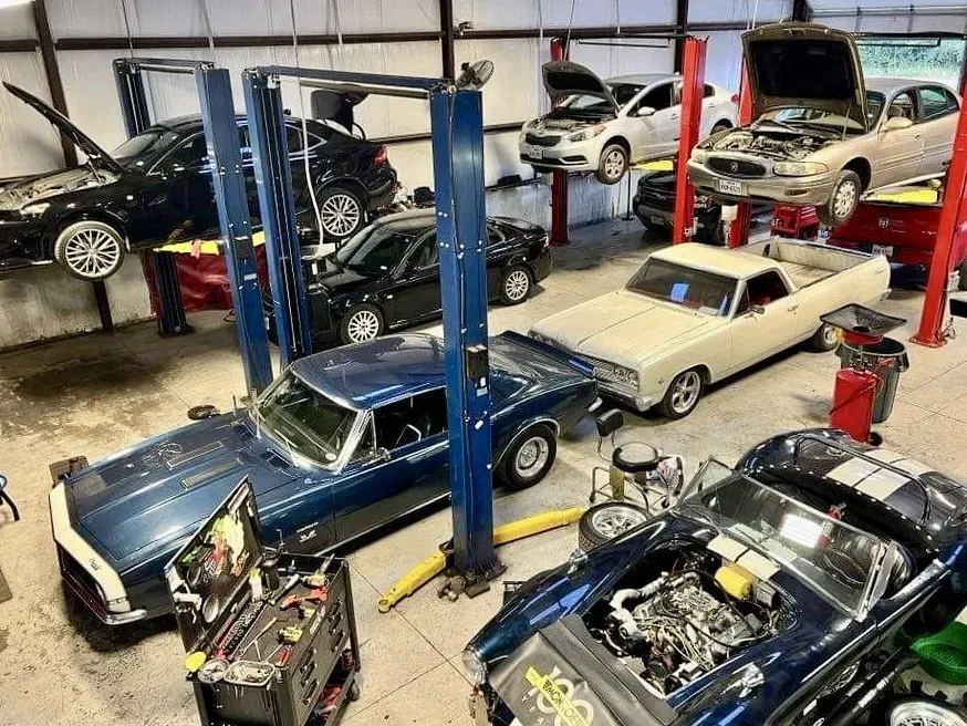 Classic cars in a workshop, with several vehicles lifted on blue car lifts. | Cruz-N-Carz
