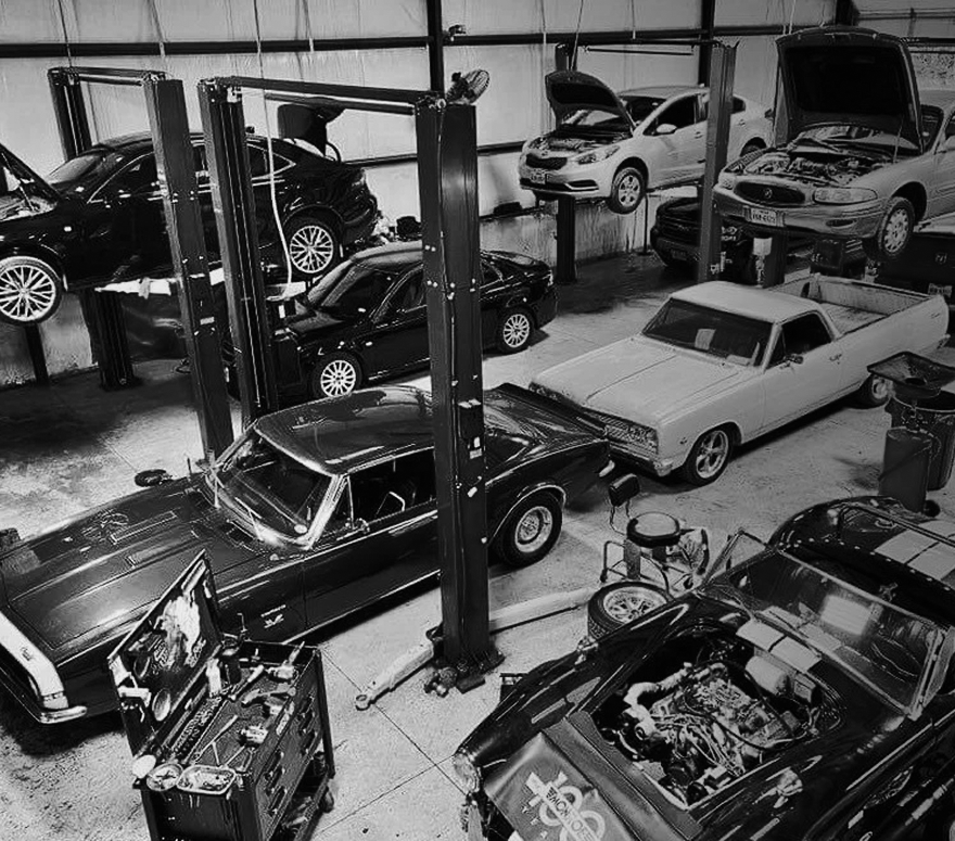 Classic cars packed in a workshop, with several lifts and a white convertible in the center. | Cruz-N-Carz