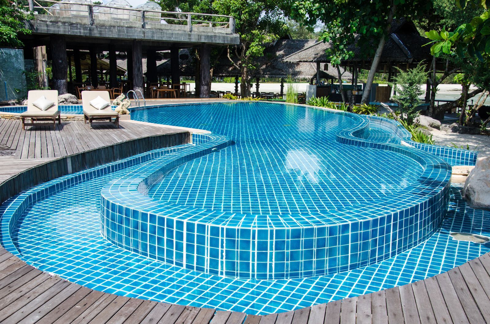 Swimming pool with blue tiles, surrounded by wooden deck.  Two lounge chairs are nearby. Trees in background.