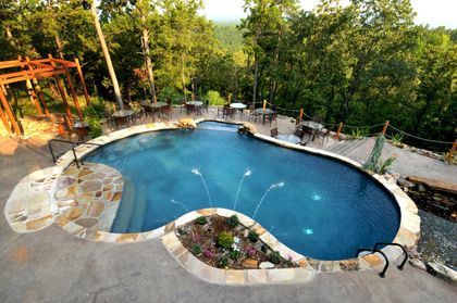 Pool with fountains and stone features, surrounded by trees and outdoor dining tables.