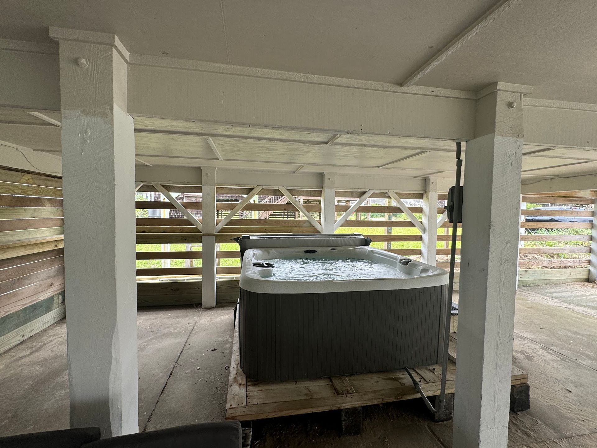 Hot tub under a covered structure supported by white pillars.